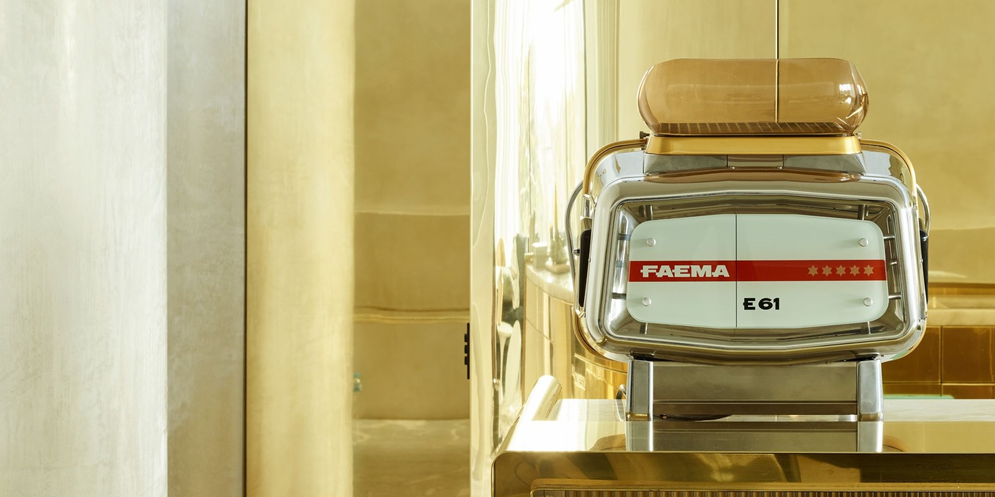 Faema E61 espresso machine on a brass counter in a sunlit interior.